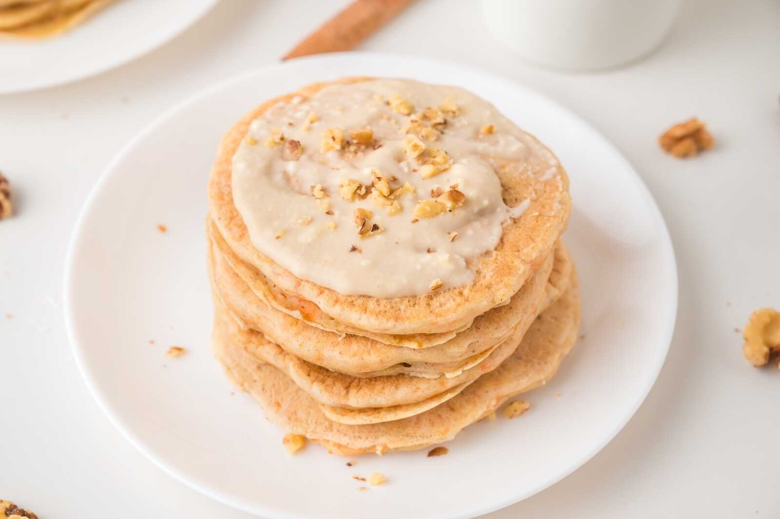 Stack of carrot cake pancakes topped with cream cheese glaze and chopped walnuts.