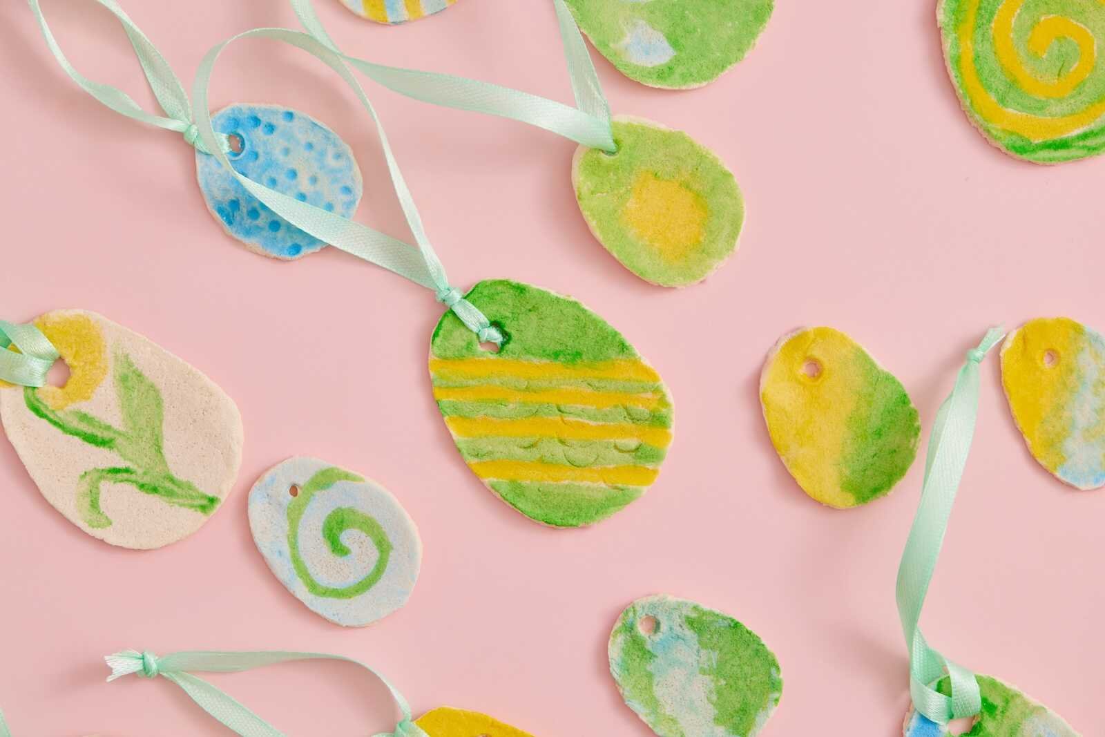 Assorted DIY salt dough Easter eggs painted in pastel colors with ribbon hangers.
