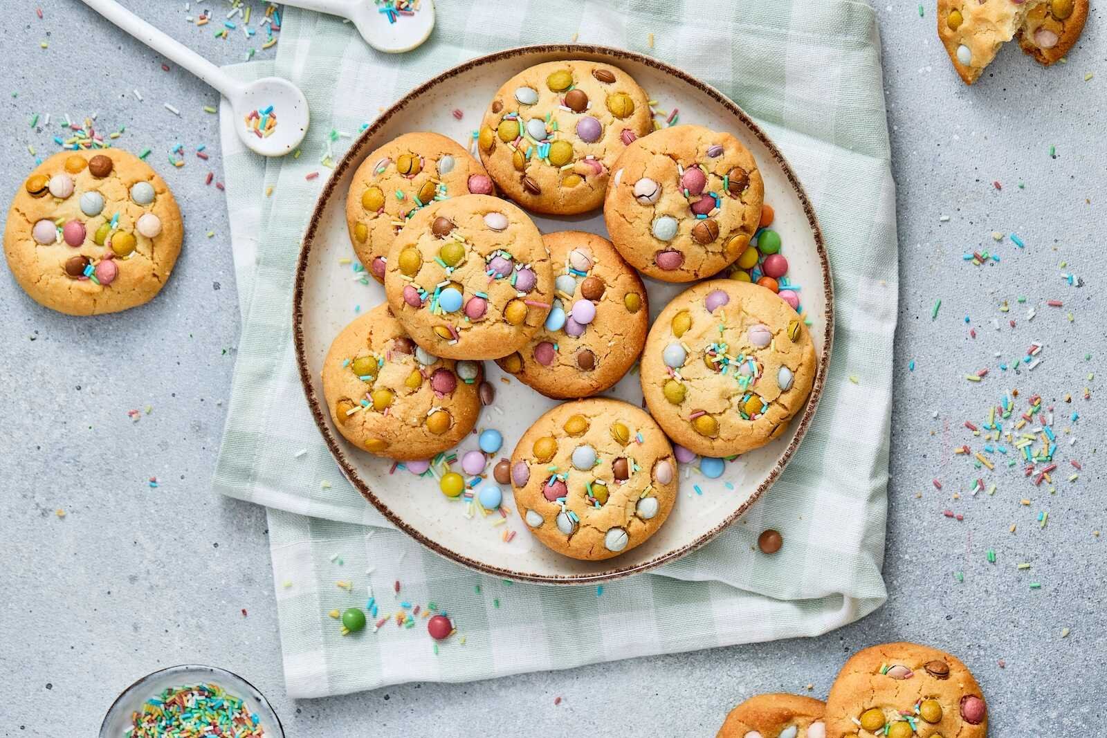 Plate of homemade Easter cookies topped with pastel candy-coated chocolates and colorful sprinkles.