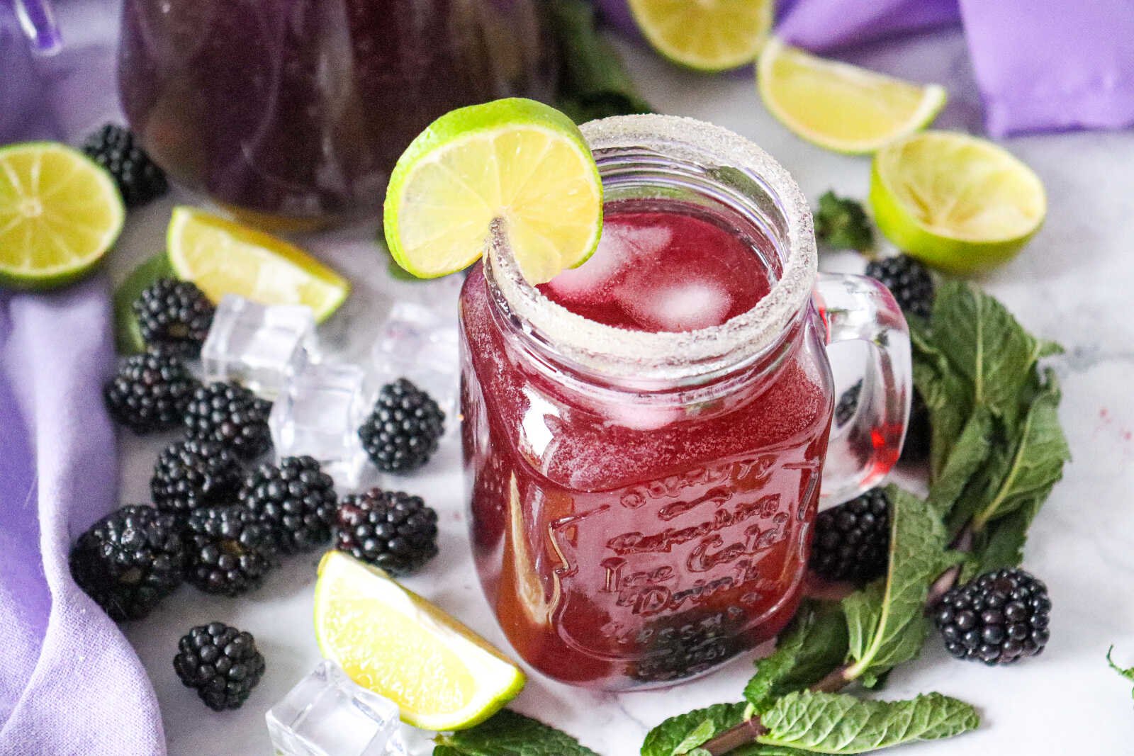 Blackberry mojito mocktail in mason jar with lime garnish, mint, and ice.