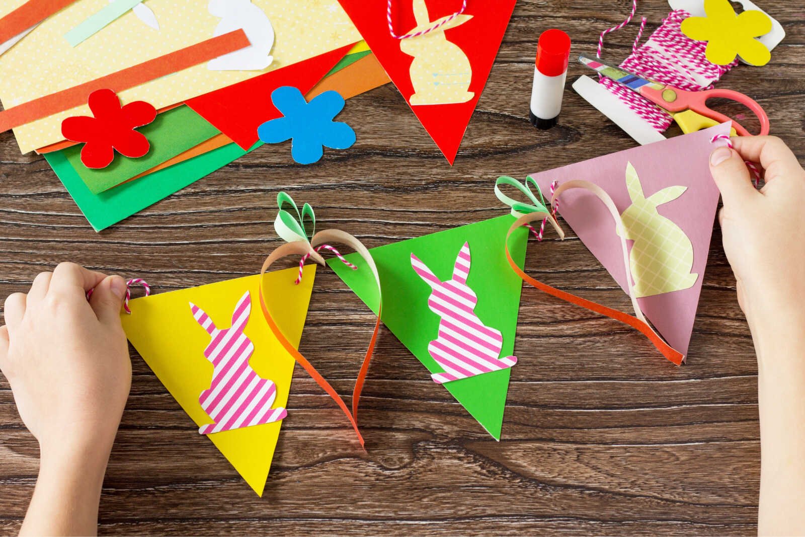 Kids assembling a colorful DIY Easter bunny banner with paper pennants, twine, and handmade carrot decorations.