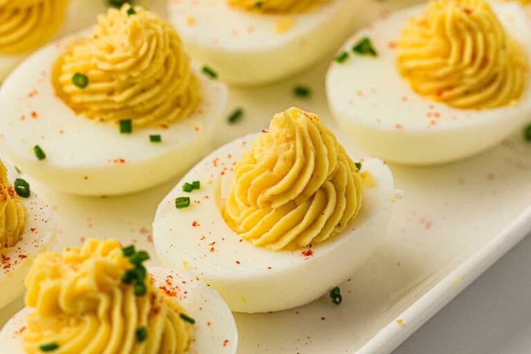 Classic deviled eggs with creamy piped filling and chive garnish arranged on a serving platter.