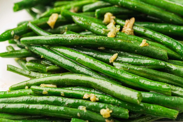 Garlic butter green beans served on a plate with minced garlic and a glossy buttery coating.